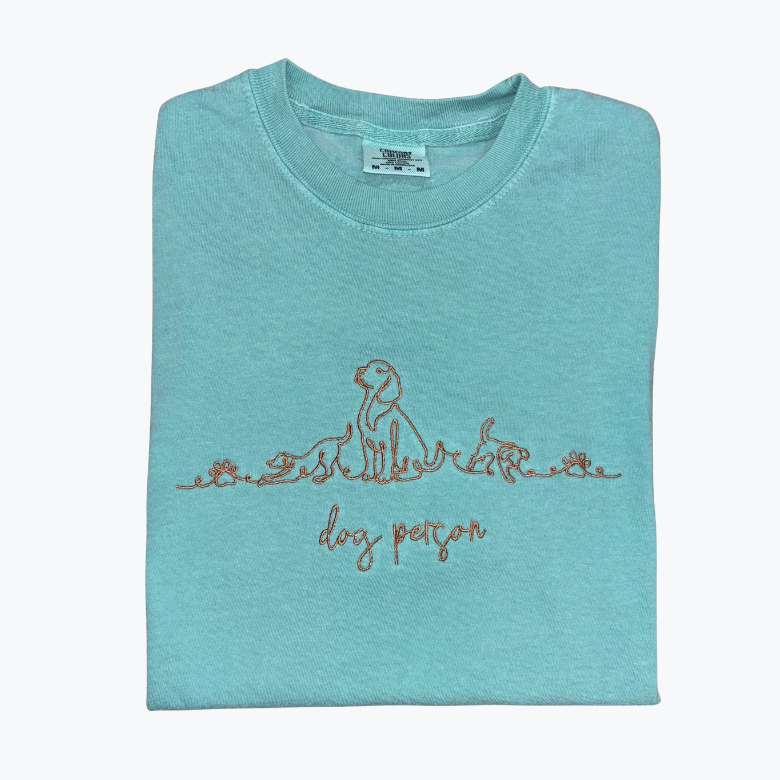 A folded light blue t-shirt with a brown line art graphic of a dog and rabbit and the text 'dog person' printed on the front, set against a plain white background.
