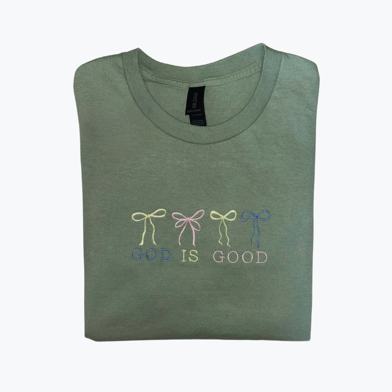 Folded green t-shirt with embroidered designs "God Is Good" with 3 bows on a white background