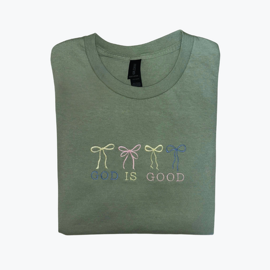 Folded green t-shirt with embroidered designs "God Is Good" with 3 bows on a white background