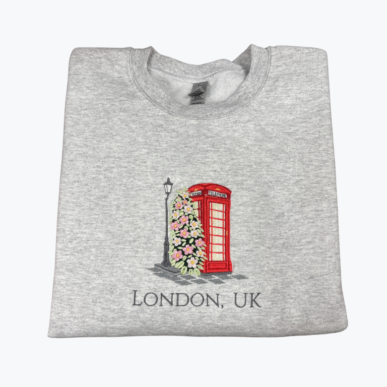 A folded heather gray t-shirt featuring a graphic of a classic red London telephone booth covered in pink flowers, with a street lamp and the text 'LONDON, UK' printed below.