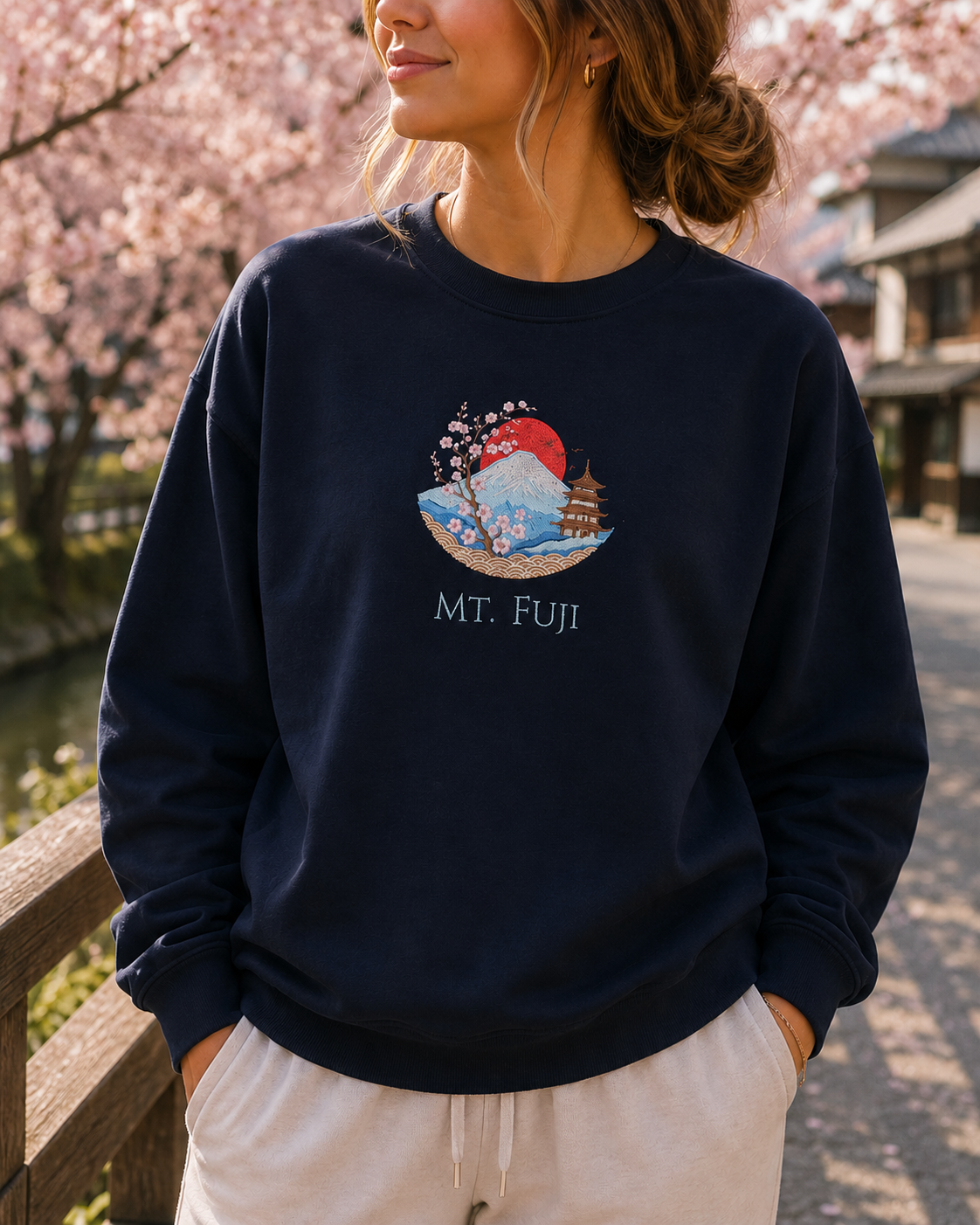 A woman wearing a navy blue crewneck sweatshirt with a colorful graphic of Mount Fuji, cherry blossoms, and a pagoda, with the text 'MT. FUJI' printed below.
