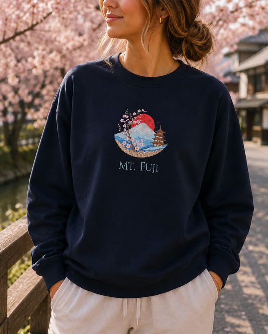 A woman wearing a navy blue crewneck sweatshirt with a colorful graphic of Mount Fuji, cherry blossoms, and a pagoda, with the text 'MT. FUJI' printed below.