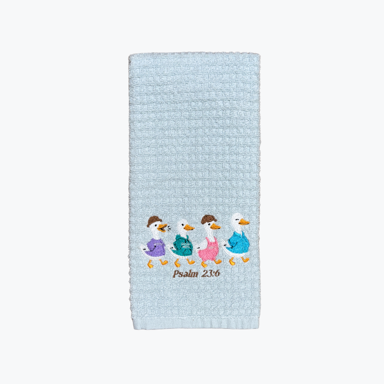 A light blue waffle-weave kitchen towel featuring an embroidered illustration of four walking ducks in colorful outfits and the text 'Psalm 23:5' below them, shown against a plain white background.