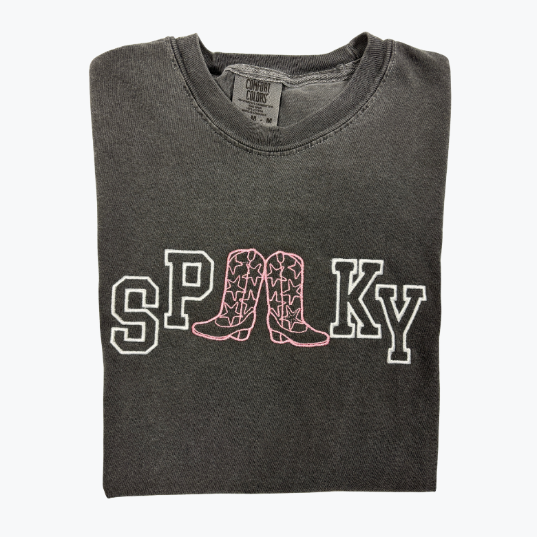A folded dark gray heather t-shirt featuring a collegiate-style 'SPOOKY' graphic across the chest, where the letter 'O' is replaced by a pair of cowboy boots in pink and white.