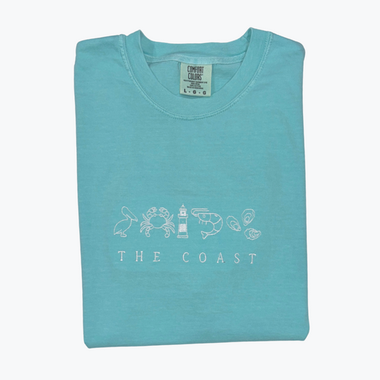 Folded turquoise t-shirt with coastal design and "The Coast" text